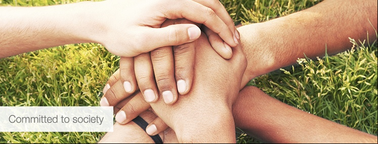 Hands intertwined on green grass, with the overprinted text "Committed to society".
